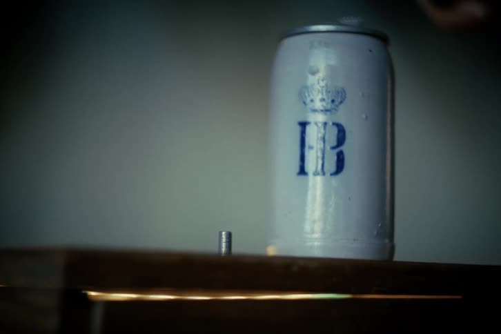 A close-up of a vintage German Hofbräuhaus beer stein sitting on a wooden shelf in a dimly lit room