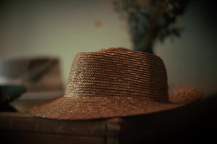 A vintage straw boater hat sits on a wooden chest in a dimly lit room, creating a nostalgic atmosphere