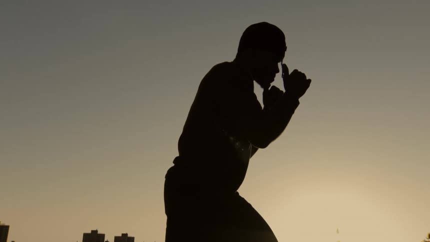 Slow motion silhouette of a man in a boxing guard position at sunset with a city skyline in the background