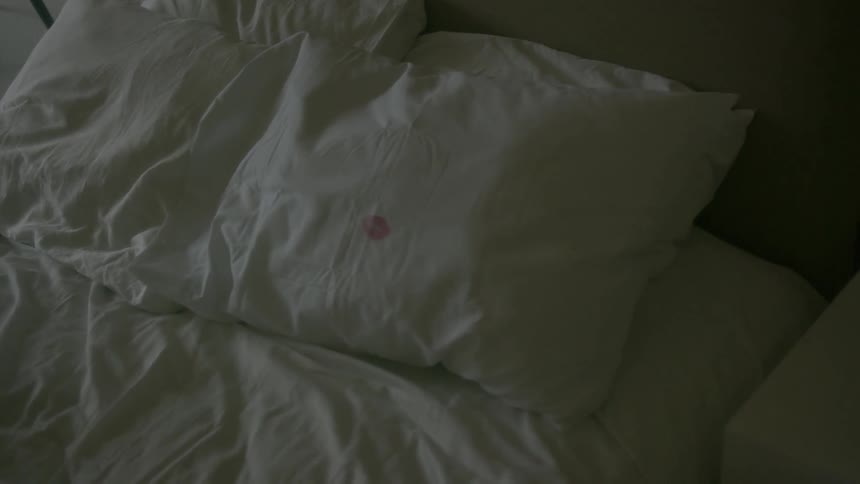 Bed with white sheets with a red stain on the pillow