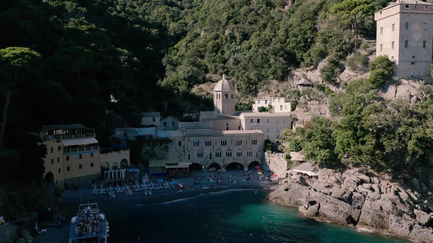 An aerial view slowly reveals the stunning San Fruttuoso Abbey and beach, nestled in a tranquil cove on the Italian Riviera