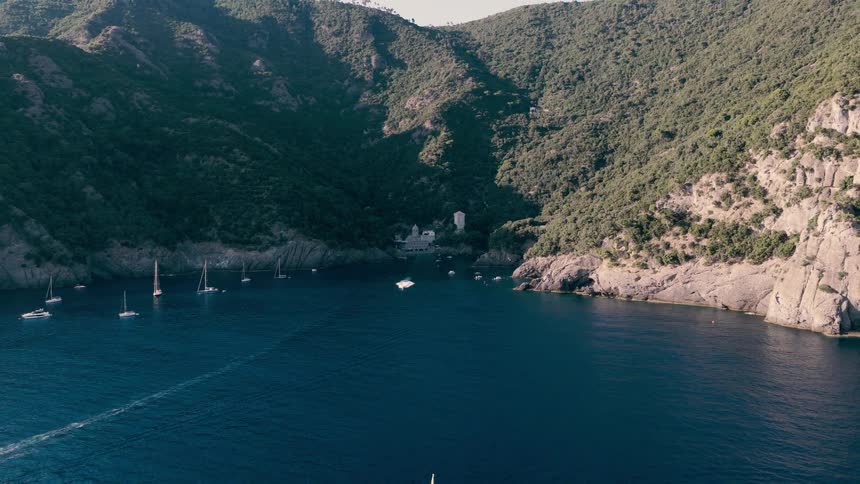 A slow aerial pullback reveals the magnificent San Fruttuoso Abbey and yachts anchored in a secluded cove along the Italian Riviera's rugged coast