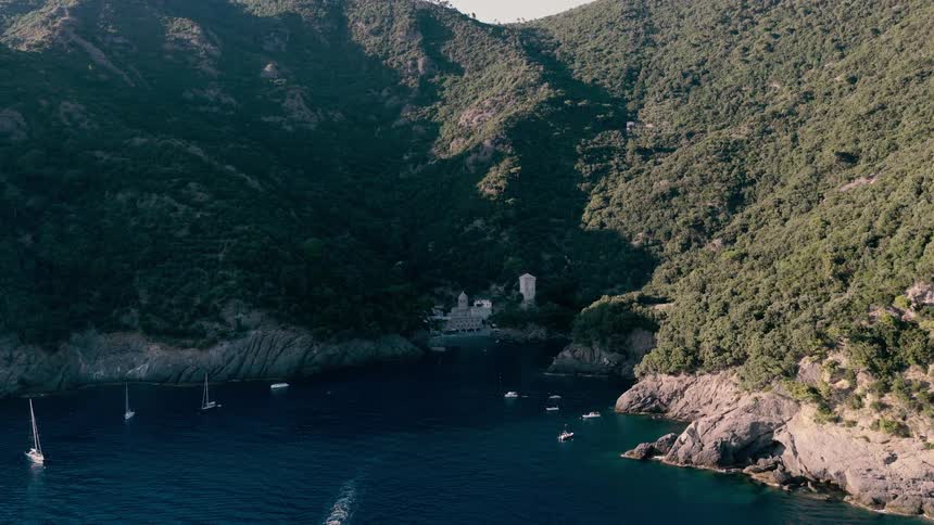 An aerial view slowly reveals the picturesque San Fruttuoso bay, with its ancient abbey and boats dotting the tranquil blue waters of the Italian Riviera