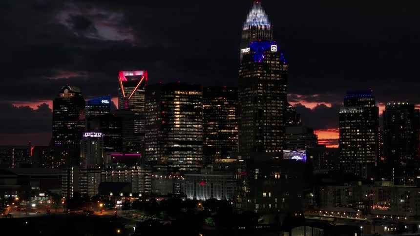 A slow aerial pullback of the glowing Charlotte, North Carolina skyline against a dramatic and colorful sunset