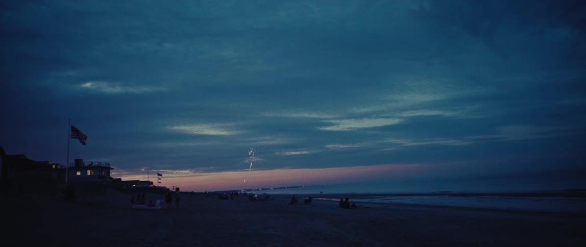 A beautiful display of fireworks lights up the cloudy twilight sky over a crowded beach