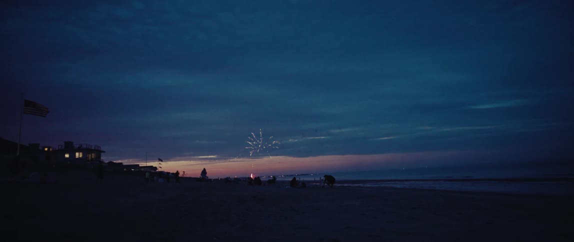Silhouetted figures on a beach watch a stunning fireworks display light up the sky at dusk