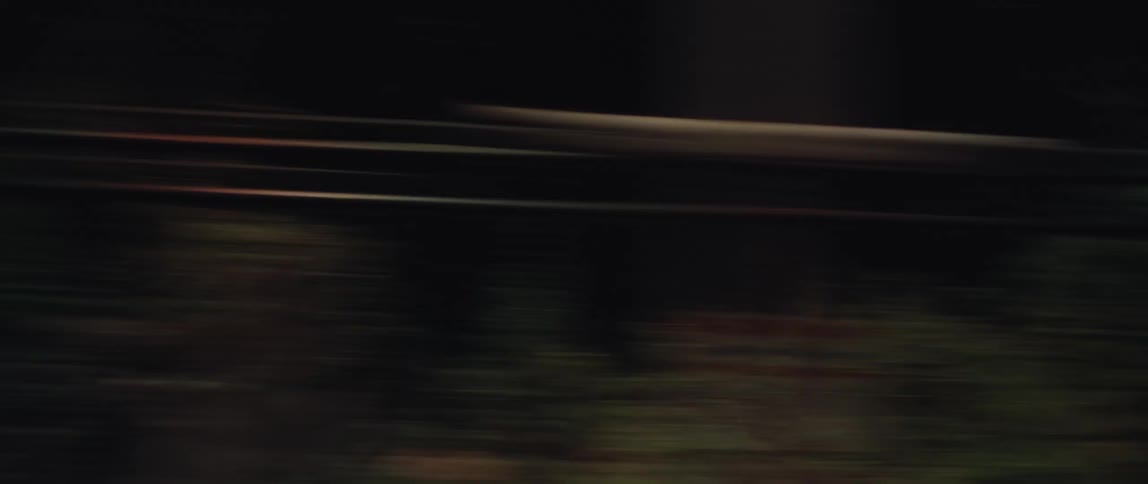 Dark, blurry point-of-view shot from a fast-moving vehicle at night, creating an abstract motion effect