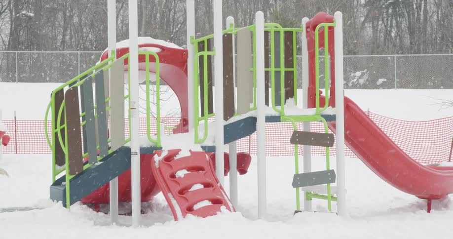 Snow falls gently on a colorful, empty children's playground covered in a blanket of fresh snow