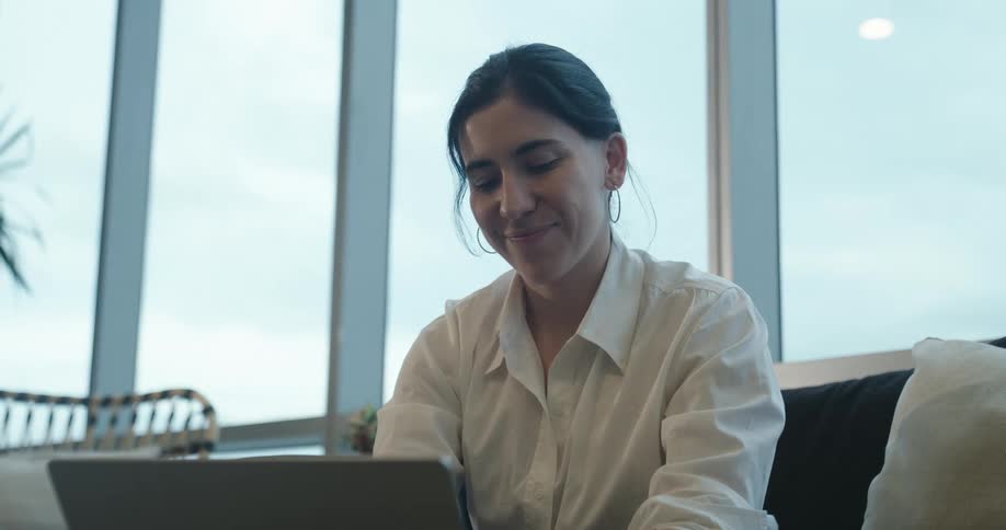 A professional woman smiles with satisfaction while working on her laptop in a contemporary high-rise office