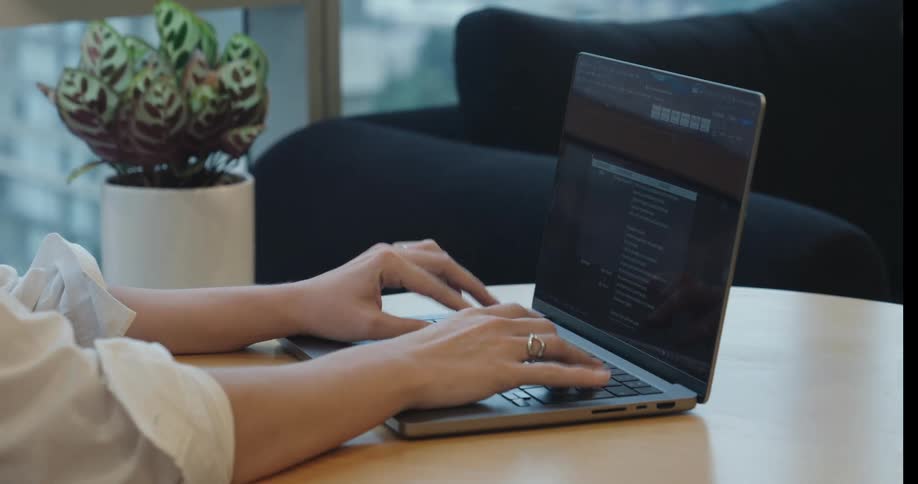 Side view close-up of a woman's hands typing on a laptop keyboard in a modern office