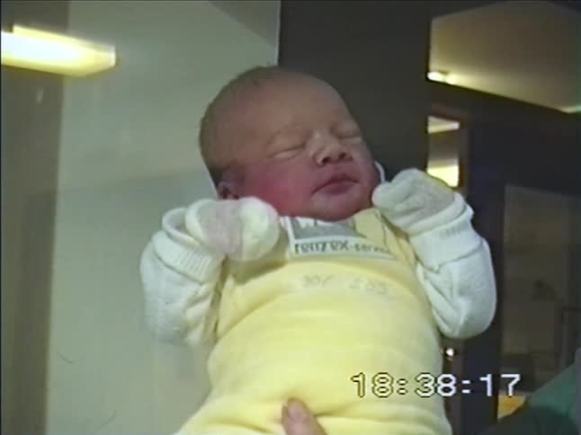 A vintage home video shows a close-up of a sweet newborn baby sleeping peacefully while being held