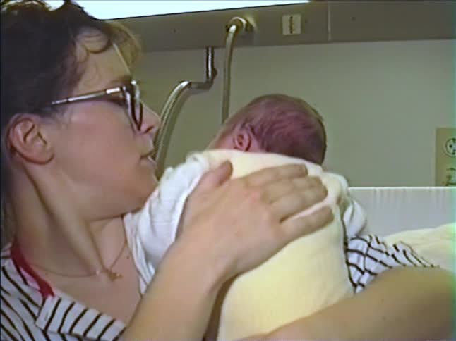 A new mother tenderly holds and soothes her newborn baby, patting its back in a hospital room