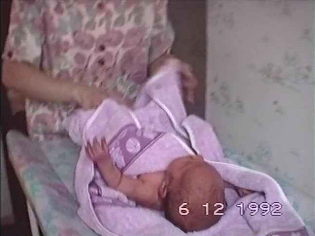 A mother carefully dries her newborn baby with a soft purple towel on a changing table in a vintage 1992 home video