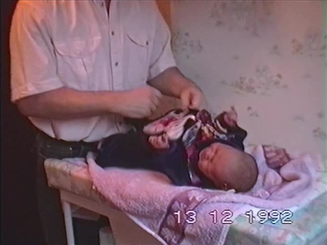 Vintage VHS footage from 1992 shows a father with a mustache gently dressing his newborn baby on a changing table