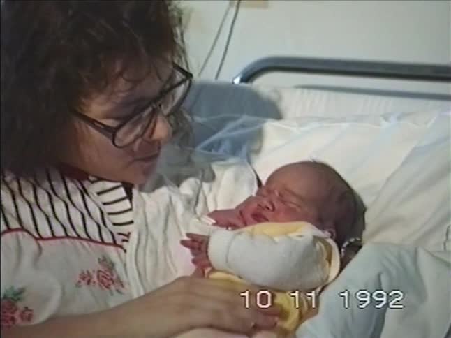 Vintage 1992 footage shows a sleepy newborn baby yawning while being lovingly held by its mother in a hospital bed