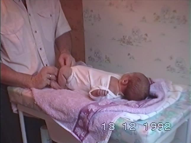 A father gently changes his newborn baby's clothes on a changing table in this authentic 1992 home movie