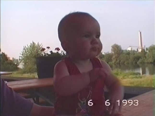 A cute baby interacts with a woman while sitting outdoors by a river in this vintage 1993 home video