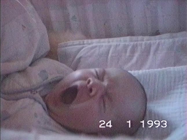 A sleepy newborn baby gives a huge yawn while lying in their crib in this sweet vintage home video from 1993