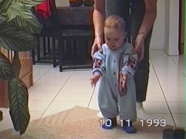 A mother helps her baby learn to walk in their home in this vintage 1993 home movie