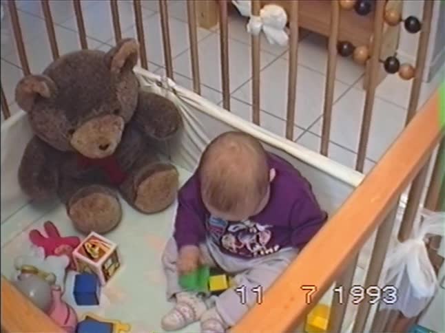 Vintage 1993 footage shows a cute baby sitting in a playpen and playing with colorful blocks and a teddy bear