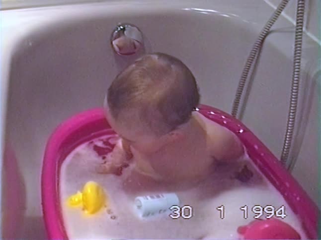 An adorable baby sits in a pink bathtub full of bubbles and toys and suddenly starts to cry in this 1994 home video