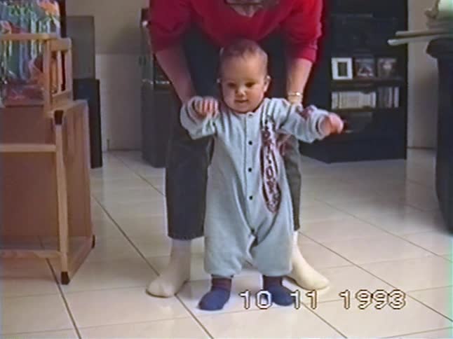 A mother helps her baby take their first wobbly steps at home in this vintage 1993 home video