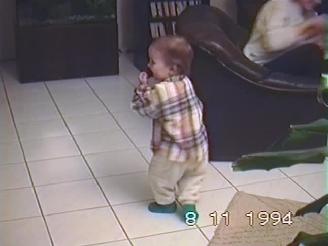 Adorable toddler in a plaid shirt dances enthusiastically before walking towards the camera in a 1994 home video