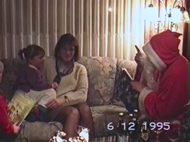 Nostalgic 1995 home video of a mother and her two young children receiving a visit from Santa Claus in their living room