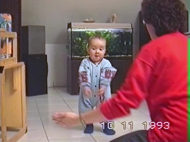 A proud mother helps her baby take its first wobbly steps before it falls to the floor and crawls away in this vintage home video from 1993