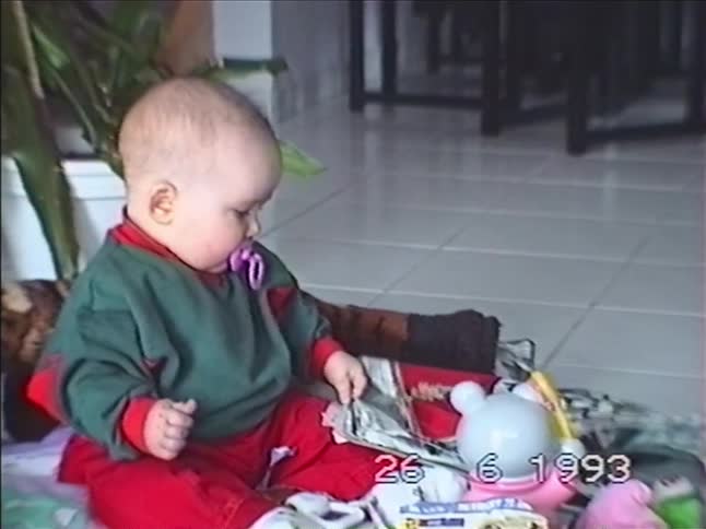 Vintage home video from 1993 shows a cute baby with a pacifier tearing apart a newspaper on the floor