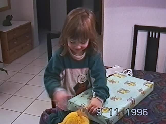 An excited little girl happily unwraps a large present at the dining table in a vintage 1996 home video