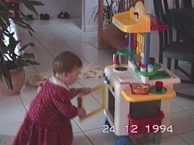 A joyful little girl in a red dress laughs with excitement over her new toy kitchen on Christmas Eve 1994