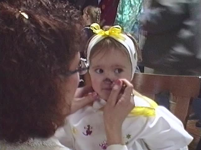 Vintage home video footage shows a woman painting a young girl's nose and whiskers for a costume party