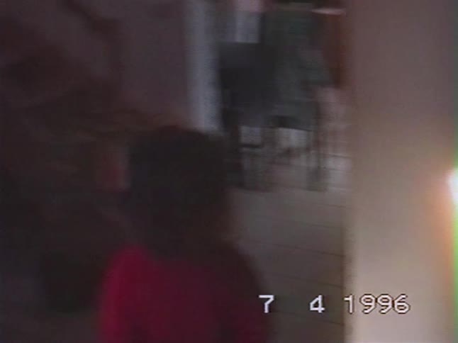 A shaky home video from 1996 captures a young child from behind standing in the hallway of a house