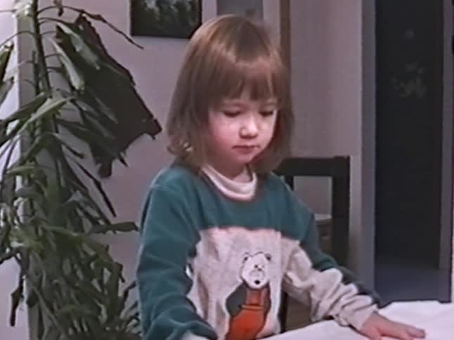 A cute young girl with brown hair concentrates while opening a gift at a table and then makes a silly face