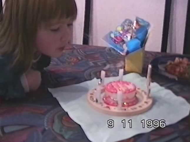 A home video from 1996 captures a young girl blowing out the candles on her pink birthday cake and smiling happily