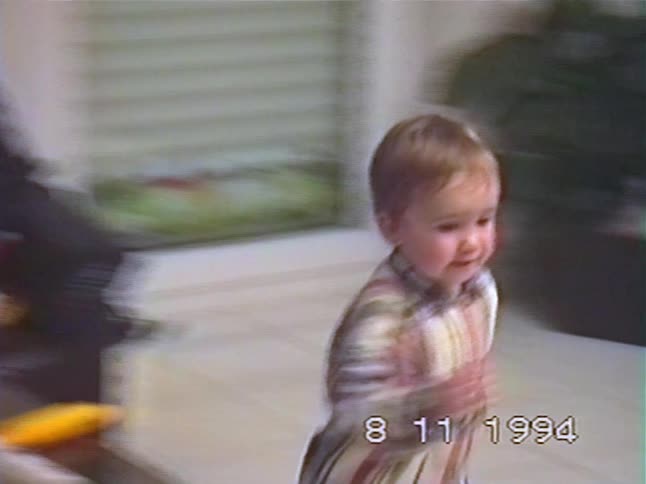 A cute toddler in a plaid shirt wanders through the house in a vintage home movie from 1994