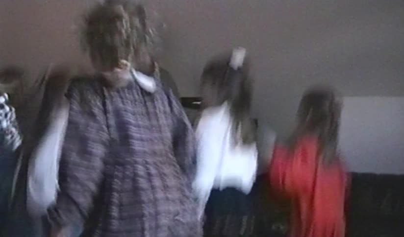 Vintage home video footage shows a group of young girls jumping and dancing with joy at a party