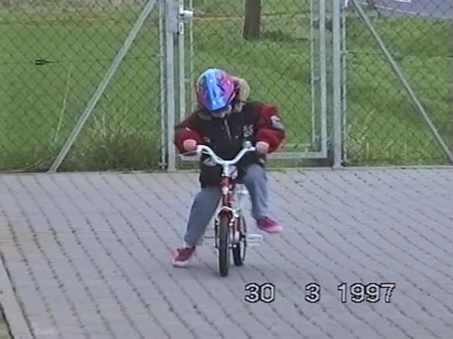 A young girl with a helmet excitedly learns to ride her first bicycle in a driveway in this nostalgic 1997 home video