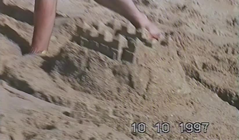 Vintage 1997 home video captures hands carefully building a sandcastle on a sunny beach