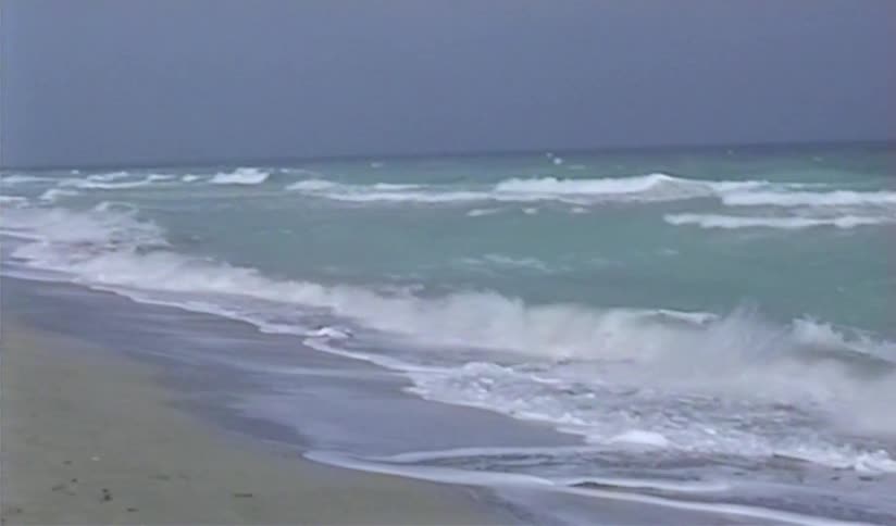 Vintage footage shows a slow pan across a stormy beach with rough ocean waves crashing onto the shore