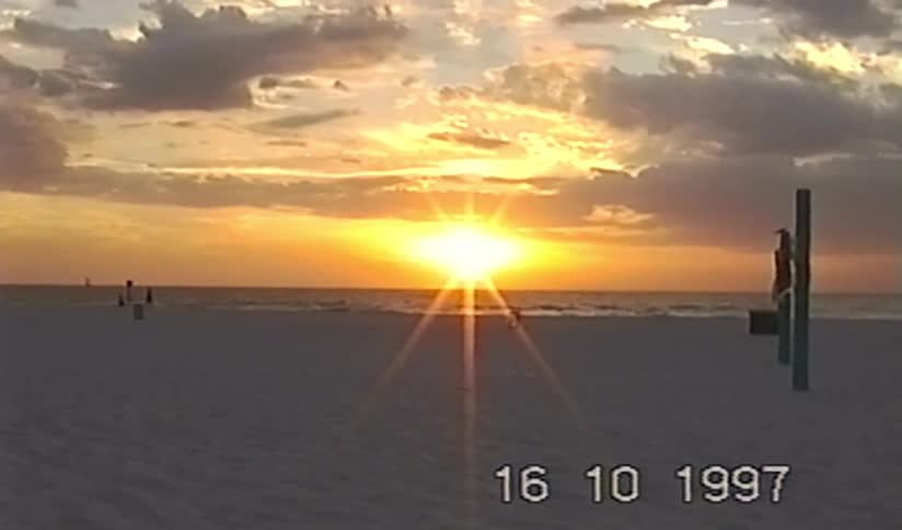 A vintage VHS recording from 1997 captures a brilliant sunset over the ocean from a sandy beach