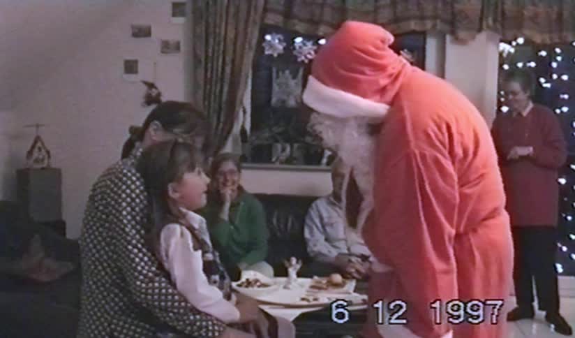 A young girl has an adorable conversation with Santa Claus while sitting on her mother's lap at a family Christmas gathering in 1997