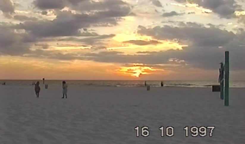 Two young girls watch a beautiful golden sunset over the ocean from a wide sandy beach in this vintage 1997 VHS clip