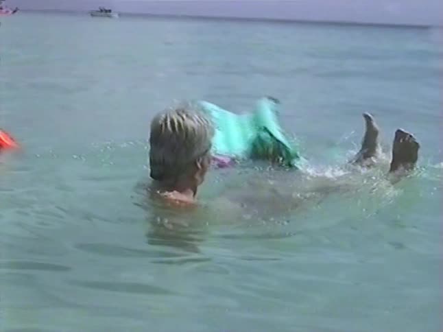 A man with a mustache and blond hair floats and swims in the ocean with an inflatable float in this vintage home movie