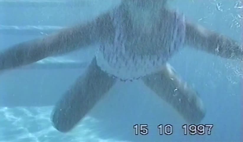 A vintage underwater shot from 1997 shows a young girl in goggles swimming playfully in a pool