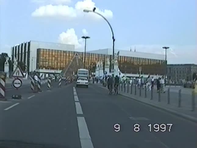 A vintage 1997 dashboard camera view driving past the Palast der Republik in Berlin with city traffic and pedestrians