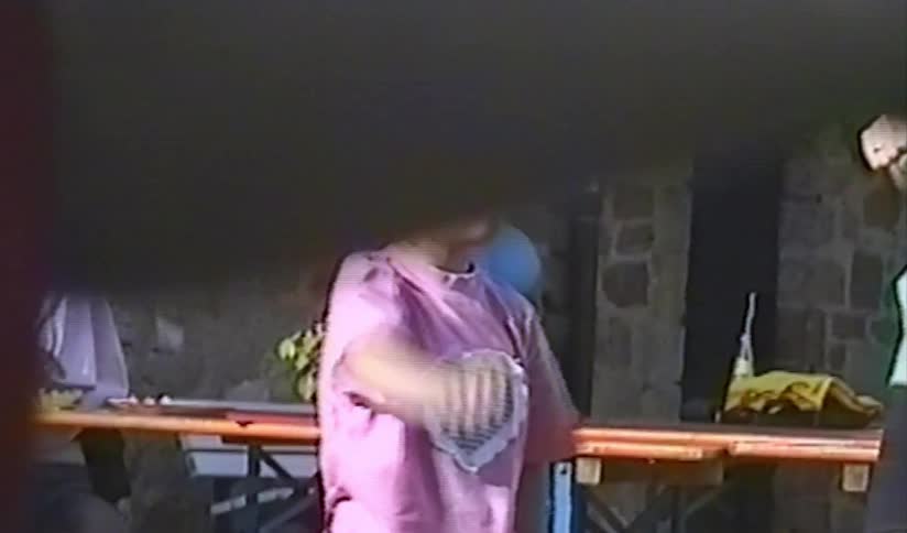 A young girl in a pink shirt and cap enthusiastically dances and performs hand gestures in a charming home video from the 1990s