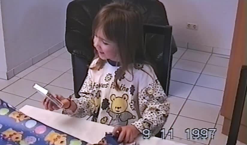 Vintage home movie footage from 1997 shows a cute little girl smiling with delight as she unwraps a present at the table