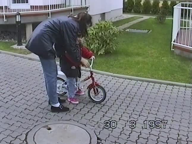 A mother teaches her young daughter how to ride a bicycle for the first time in their driveway in this authentic 1997 home video